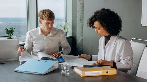 two people sitting together, reading through documents